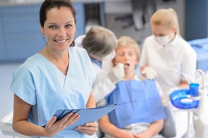 Dental assistant in the foreground with a dentist working on a patient in background